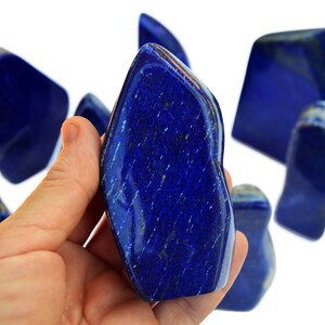 May include: A collection of polished, deep blue lapis lazuli stones. The stones are various shapes and sizes, with some having a more pointed shape and others being more rounded. The stones are smooth and have a shiny finish.