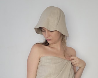 Puede incluir: Una mujer con un sombrero de cubo de lino beige y un vestido de envoltura de lino beige.