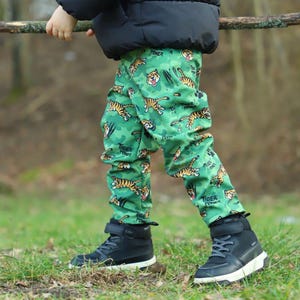May include: A child wearing black pants with a green and orange tiger print and the words "Tiger Power" repeated on the pants. The child is wearing black high-top sneakers.