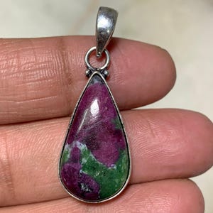 Pode incluir: Um pingente em forma de gota com uma argola de prata. O pingente apresenta uma pedra preciosa polida com uma mistura de cores vermelho escuro e verde. A pedra preciosa é definida em uma moldura de prata.