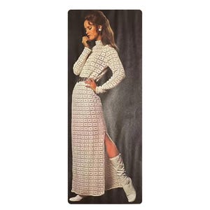 May include: An ivory crochet dress with long sleeves, a high neckline, and a thigh-high slit. The dress is cinched at the waist with a dark belt. The model is wearing white boots and earrings.