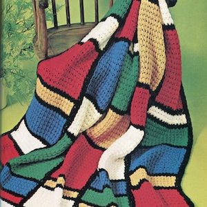 May include: A vibrant, hand-crocheted blanket draped over a wooden chair. The blanket showcases a patchwork design with striking blocks of red, blue, green, yellow, white, and brown, edged in black. A cosy home decor item.