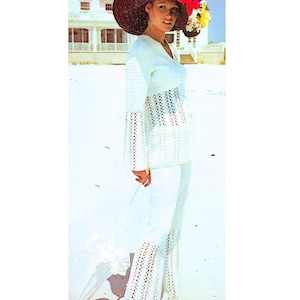 May include: A white crochet outfit, including a long-sleeved top and flared pants, is shown. The top has a V-neck and openwork detailing. The outfit is paired with a wide-brimmed hat and a white parasol, creating a vintage beach look.