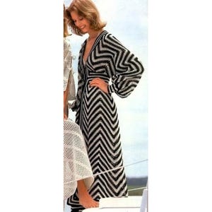 May include: A black and white chevron patterned crochet dress with long sleeves and a V-neck. The dress is floor-length and appears to be handmade. A second person is partially visible, wearing a white crochet garment.