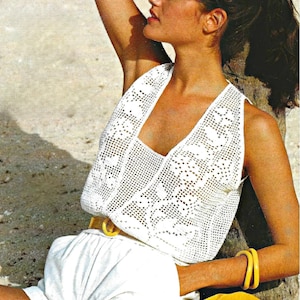 Könnte beinhalten: Ein weißes Häkeltop mit V-Ausschnitt. Das Top wird mit weißen Shorts und einem gelben Gürtel kombiniert. Gelbe Armreifen sind am Arm zu sehen. Das Bild hat eine Vintage-Ästhetik.