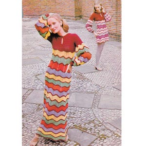 May include: A woman wearing a long, colorful crochet dress with a chevron pattern in shades of red, yellow, green, and purple. The dress has long sleeves and a keyhole neckline. Another woman is wearing a shorter dress with a similar pattern.