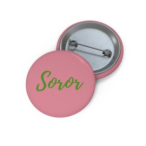 Op de afbeelding: Een roze knoop met het woord "Soror" in groene cursieve letters.