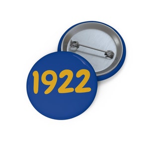Op de afbeelding: Een blauwe knop met een gele 1922 erop.