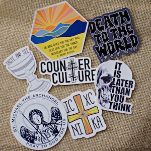 May include: A set of nine stickers with various designs and sayings. The stickers are printed on white paper with black, blue, yellow, orange, and red ink. The stickers include a sunset scene, a skull, a chalice, a cross, and a saint. The text on the stickers includes "Taste and See", "Death to the World", "Counter Culture", "St. Michael the Archangel", "IC XC NIKA", and "It is Later Than You Think".