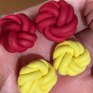 May include: Four small, handmade clay ornaments in the shape of a knot. Two are red and two are yellow.