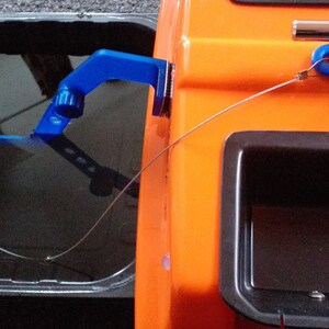 May include: A blue fishing rod holder attached to a small orange boat. The rod holder has a black knob and a blue hook. The boat has a black storage compartment.
