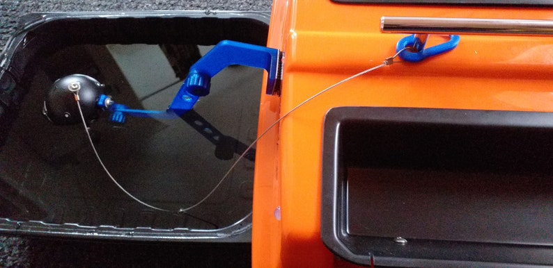 May include: A blue fishing rod holder attached to a small orange boat. The rod holder has a black knob and a blue hook. The boat has a black storage compartment.