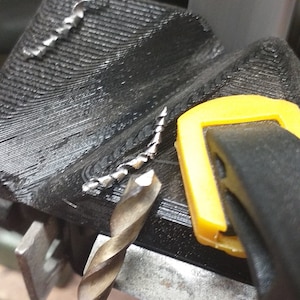 Puede incluir: Primer plano de una broca que se está afilando en una muela. La broca se mantiene en su lugar mediante una abrazadera amarilla y negra. Se pueden ver virutas de metal en la superficie de la muela.