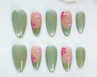 May include: A set of ten artificial nails in a variety of sizes. The nails are primarily a light green color with a metallic sheen. Some nails feature a pink floral design on a nude base, while others are solid green.