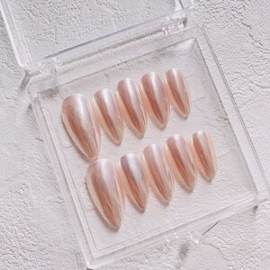May include: A set of ten pearly white, almond-shaped false nails in a clear plastic case. The nails are arranged in two rows of five.