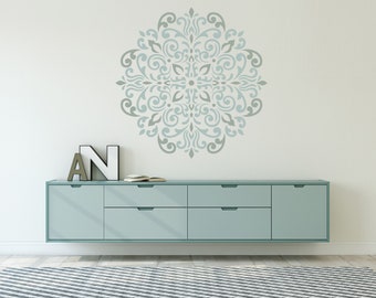 May include: A light blue wall with a large, intricate, gray and blue mandala stencil design. Below the stencil is a light blue dresser with four drawers and a light blue rug with white stripes.