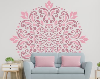 May include: A pink and white mandala stencil with a decorative floral design. The stencil is on a white wall above a light blue sofa with pink pillows.