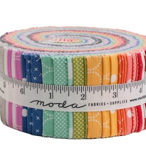 Könnte beinhalten: Ein gerolltes Bündel bunter Stoffstreifen, das ein Spektrum an Farbtönen von Rosa und Blau bis Grün, Gelb und Rot zeigt. Der Stoff ist mit einem Maßband mit der Aufschrift "moda fabrics supplies" umwickelt.