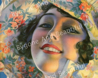 May include: A woman with dark hair and bright blue eyes smiles while wearing a white hat with a floral pattern. The hat has pink, orange, yellow, and blue flowers.