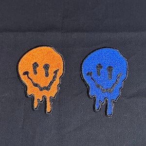 May include: Two iron-on patches with a dripping smiley face design. One patch is orange and the other is blue.