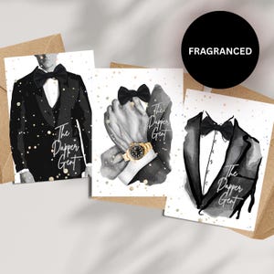Può includere: Tre biglietti di auguri con illustrazioni ad acquerello di uno smoking, un papillon e mani maschili con un orologio d'oro. I biglietti hanno il testo "The Dapper Gent" e sono su uno sfondo chiaro con pagliuzze dorate. Un cerchio nero con la scritta "FRAGRANCED" è in alto a destra.