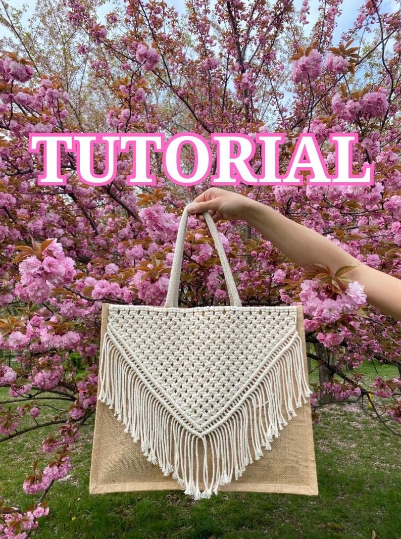 May include: A white macrame tote bag with fringe details, held in front of a pink cherry blossom tree. The bag has a brown jute base and is made with a knotted design. The text "TUTORIAL" is superimposed on the image.