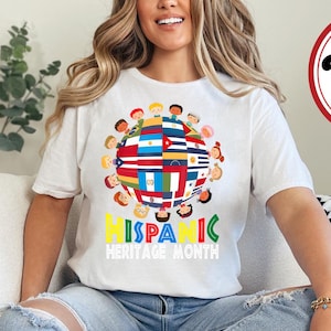 May include: White t-shirt with a colorful graphic of a globe with children holding hands around it. The globe is made up of different flags representing Hispanic countries. The text "HISPANIC HERITAGE MONTH" is printed below the globe.