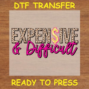 May include: Ready to press iron-on transfer with the text "Expensive & Difficult" in pink and black lettering with a gold dollar sign and leopard print background.