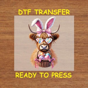 May include: A DTF transfer design featuring a brown Highland cow with pink bunny ears, heart-shaped sunglasses, and a basket of colorful Easter eggs. The design says "DTF Transfer" and "Ready to Press".