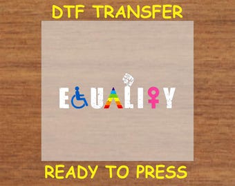 May include: A white iron-on transfer sheet with the word "EQUALITY" in black letters with a rainbow triangle, a pink female symbol, a blue wheelchair symbol, and a black fist symbol. The text "DTF TRANSFER" is at the top of the sheet and "READY TO PRESS" is at the bottom.