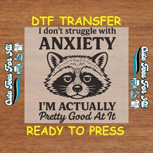 May include: A DTF transfer featuring a raccoon illustration with the text "I don't struggle with ANXIETY, I'M ACTUALLY Pretty Good At It, READY TO PRESS." The design is in black and white with yellow text accents, perfect for apparel.