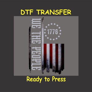 May include: A distressed American flag design with the words "We The People" and "1776" in white. The design is ready to be pressed onto a t-shirt or other fabric.