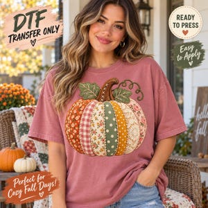 May include: A dusty rose t-shirt featuring a large, central graphic of a patchwork pumpkin. The pumpkin is composed of various fabric patterns including floral, gingham, polka dot, and lace textures, with a brown stem and green leaves.