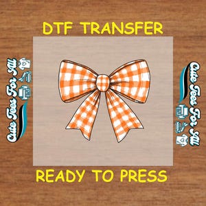 May include: A DTF transfer featuring a large, orange and white gingham bow. The words "DTF TRANSFER" and "READY TO PRESS" are in yellow text above and below the bow. The words "Cute Tees For All" are on the left and right sides.