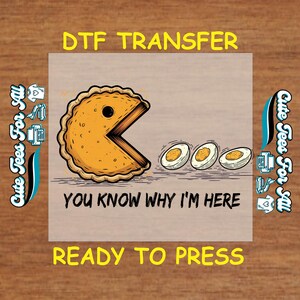 May include: A DTF transfer design featuring a pie-shaped character with a bite taken out, resembling Pac-Man, and three egg halves. The text reads "YOU KNOW WHY I'M HERE" and "READY TO PRESS". The design is on a light brown background.