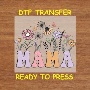 May include: A ready-to-press iron-on transfer with the word "MAMA" in colorful, retro-style letters. The letters are surrounded by a floral design with pink, purple, and yellow flowers.