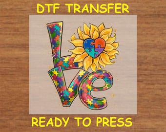 May include: A DTF transfer design featuring the word "LOVE" in colourful puzzle pieces with a sunflower and a puzzle piece heart in the centre. The text "READY TO PRESS" is below the design.