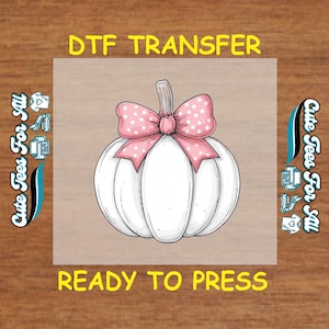Puede incluir: Transferencia DTF con una calabaza blanca con un lazo rosa con lunares. Las palabras "DTF TRANSFER" y "READY TO PRESS" están en amarillo. La imagen está sobre un fondo marrón claro. El texto "Cute Tees For All" está a los lados.