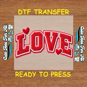 May include: A red and white DTF transfer with the word "LOVE" in a varsity-style font. The transfer includes two red hearts and the text "READY TO PRESS". The phrase "Cute Tees For All" is printed on the left and right sides.