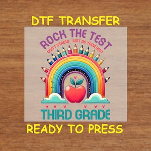 May include: A rainbow-colored design with pencils forming the arc of the rainbow. The text "Rock the Test Don't Stress. Just Do Your Best" is above the rainbow. A red apple with a green leaf is in the center of the rainbow. The text "Third Grade" is below the rainbow. The text "Ready to Press" is below the text "Third Grade".