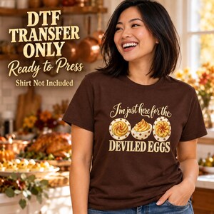 May include: A dark brown short-sleeve t-shirt featuring a graphic of three deviled eggs and the text "I'm just here for the DEVILED EGGS". The image includes overlay text stating "DTF TRANSFER ONLY Ready to Press Shirt Not Included".