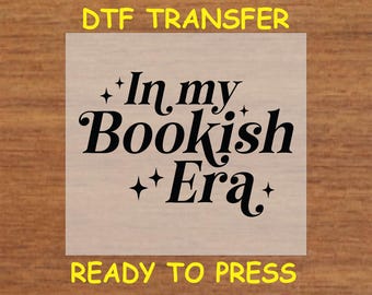 May include: A ready-to-press iron-on transfer sheet with the text "In my Bookish Era" in black cursive font with small stars on either side of the text.