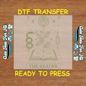 May include: A green and white DTF transfer design featuring a rose, a snake, a book, and a crystal. The design says "The Reader" and is ready to press.
