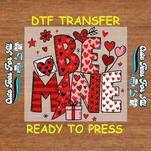 May include: A Valentine's Day DTF transfer design with the words "BE MINE" in red and pink, decorated with hearts, stars, and a gift box. The design includes the text "READY TO PRESS" and "Cute Tees For All".