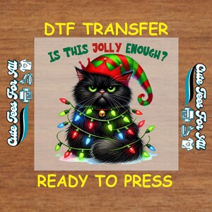 May include: A DTF transfer featuring a black cat wearing a Christmas elf hat and wrapped in colorful Christmas lights. The text "IS THIS JOLLY ENOUGH?" and "READY TO PRESS" are included. The image is on a light brown background.