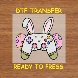 May include: A white game controller with bunny ears and pink and purple accents. The text "DTF TRANSFER" and "READY TO PRESS" is on the image.