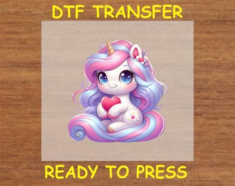 May include: A DTF transfer sheet featuring a cartoon unicorn with pink and blue hair holding a pink heart. The sheet says "DTF Transfer" at the top and "Ready to Press" at the bottom.