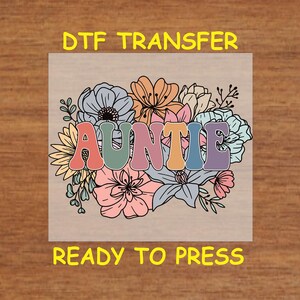 May include: DTF transfer with the word "AUNTIE" in colorful bubble letters, surrounded by a floral design in pastel colors. The text "READY TO PRESS" is below the design.
