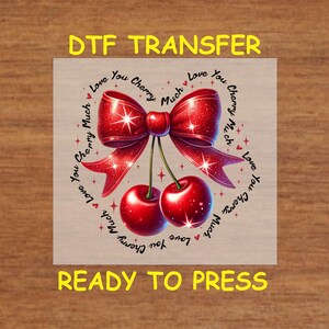 May include: A DTF transfer design featuring a pair of glossy red cherries and a matching bow. The words "Love You Cherry Much" are arranged in a heart shape around the bow and cherries. The text "DTF TRANSFER" and "READY TO PRESS" are also present.