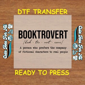 May include: A brown wood background with a white square in the center. The square has the text "DTF TRANSFER" in yellow at the top, "BOOKTROVERT" in black at the center, and "READY TO PRESS" in yellow at the bottom. The text "[book-too-vert-noun]" is in black below "BOOKTROVERT". The text "A person who prefers the company of fictional characters to real people" is in black below the definition. The square is surrounded by two blue and white logos that say "Cute Tees For Sal".
